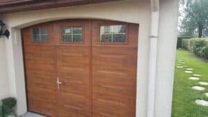 porte de garage sectionnelle en aluminium isolé coloris chêne doré avec hublots et portillons intégré